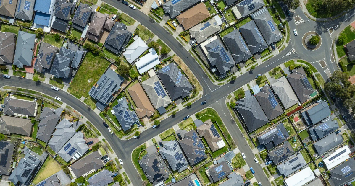 Aerial view of a suburban neighborhood with solar panels on many rooftops along curving streets.