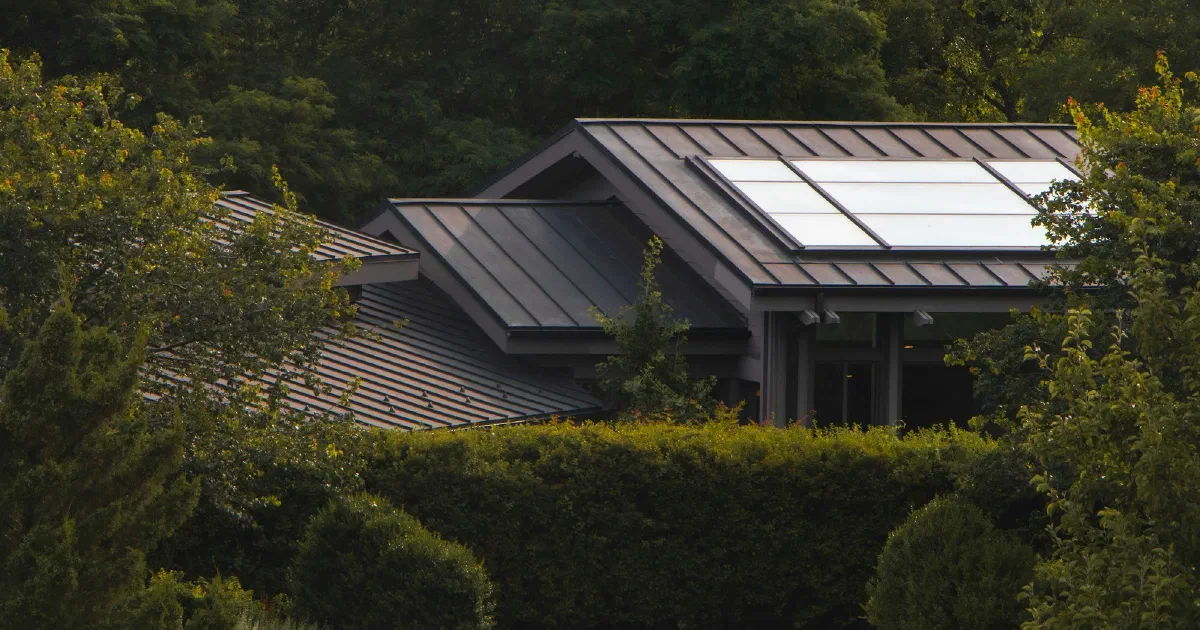 House with a metal roof and rooftop solar panels surrounded by dense green trees.