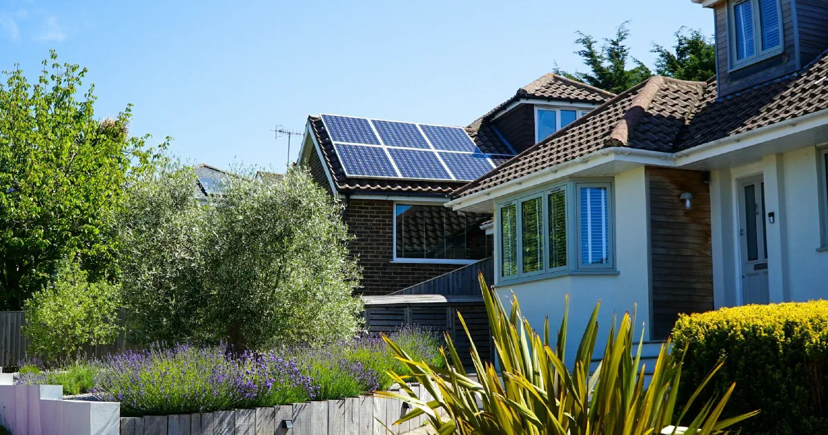 House with solar panels on a tiled roof behind a garden with lavender and shrubs.