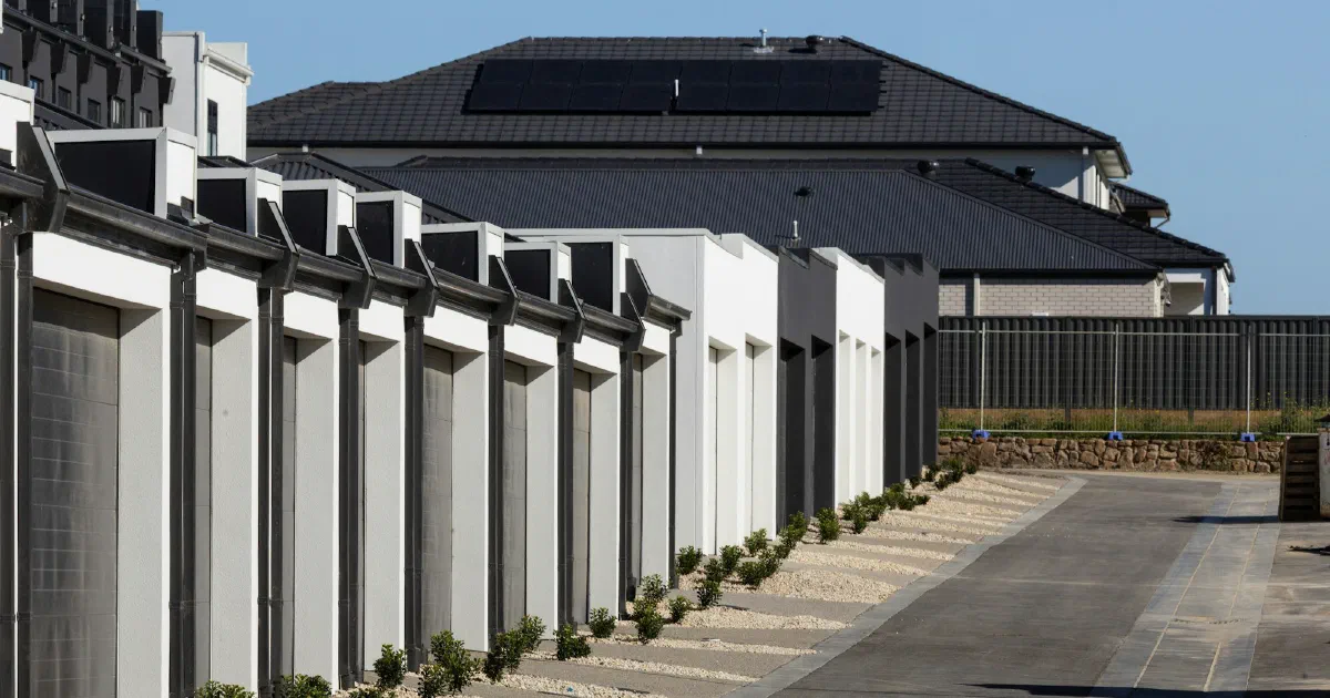 Row of modern townhouses with garages and dark solar panels on a larger roof behind.
