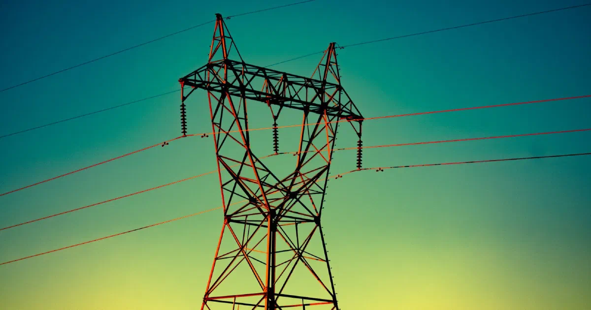 Steel transmission tower and power lines against a green and yellow evening sky.