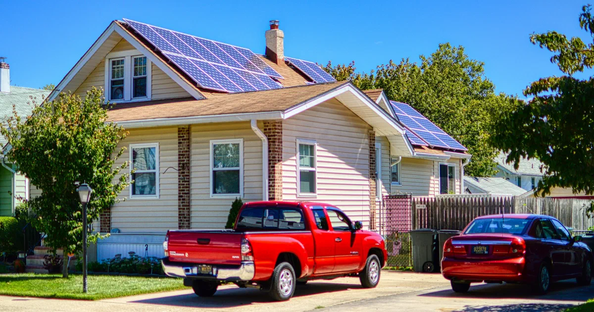 Two-story house with solar panels on its roof and a red pickup truck parked in the driveway.