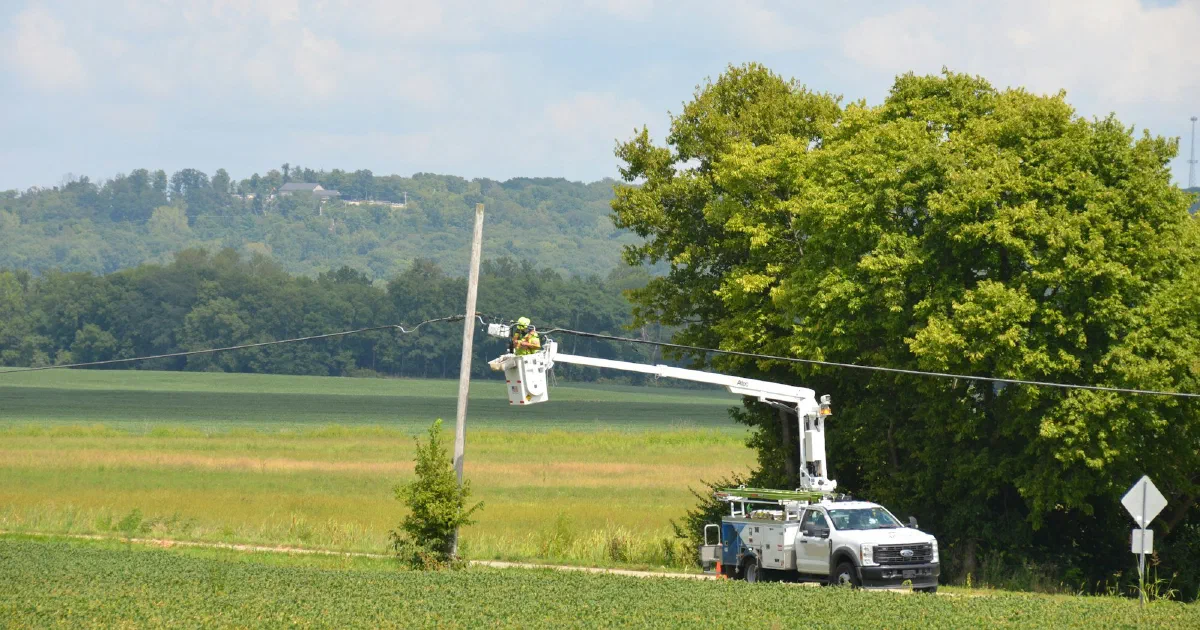 Utility worker in a bucket truck repairing a power line beside a green field.