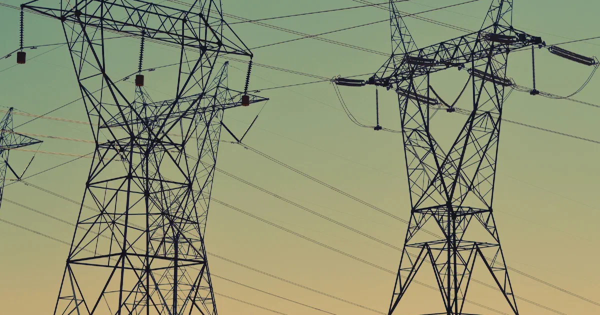 Close view of steel transmission towers and power lines against a green and yellow sky.