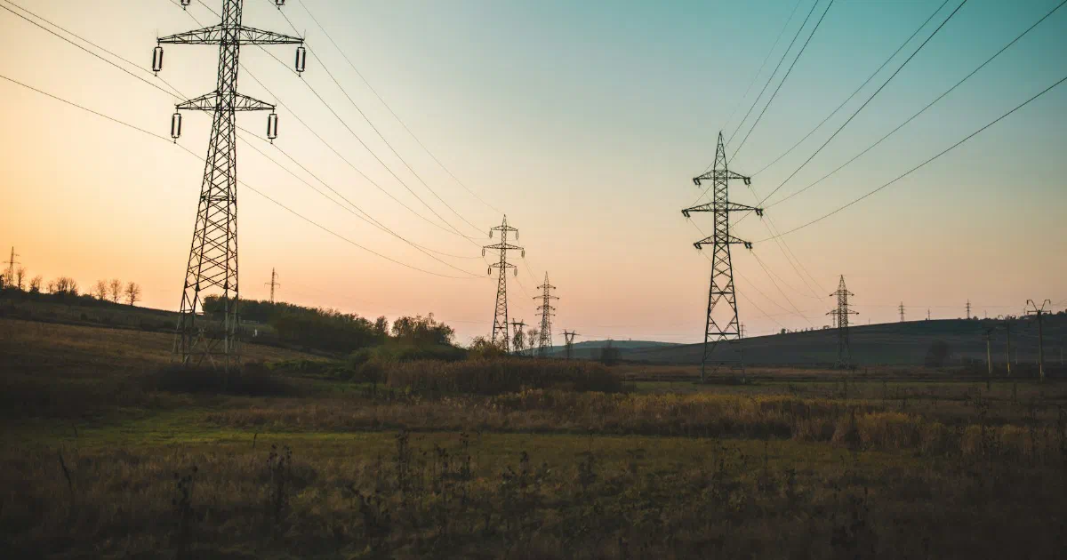 Line of transmission towers crossing open fields at dusk.