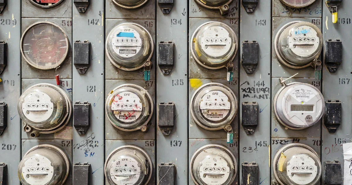 Wall of round analog electric meters mounted in rows on a gray metal panel.