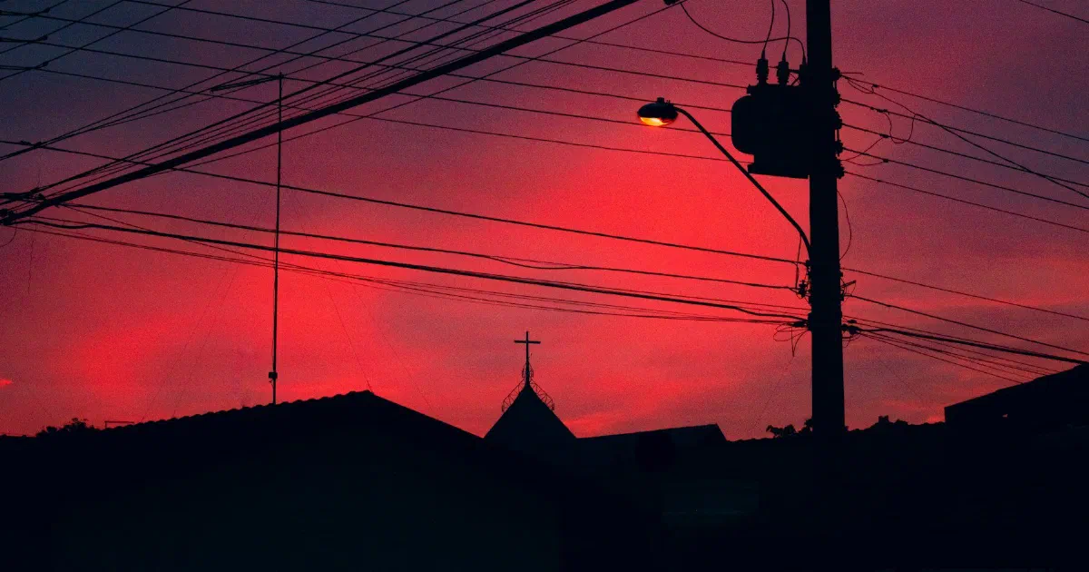 Utility pole, transformer and power lines silhouetted against a deep red sky.