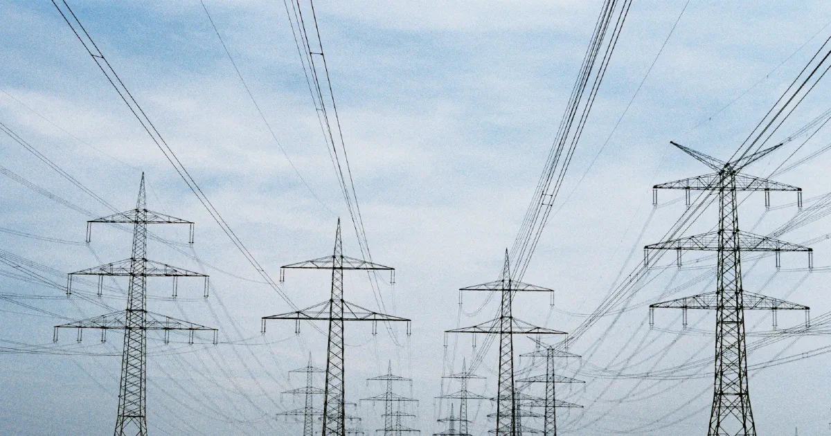 Rows of transmission towers and power lines crossing a brown farm field.