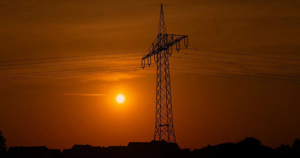 Transmission tower silhouetted against an orange sky with the sun low on the horizon.