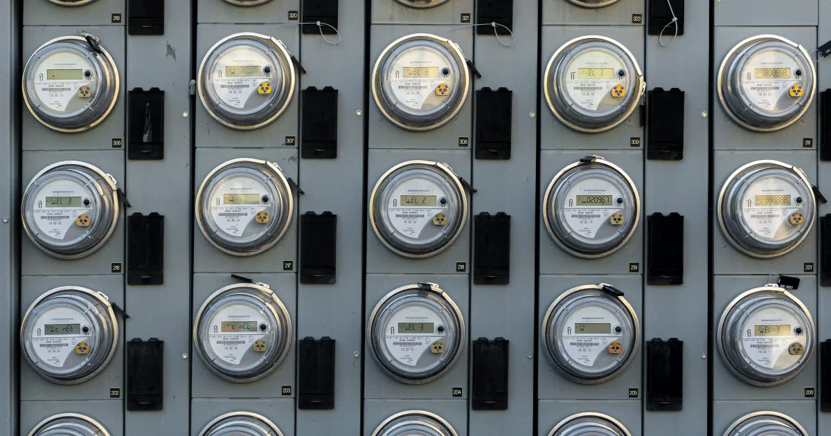 Grid of electric meters mounted on a gray metal panel wall.