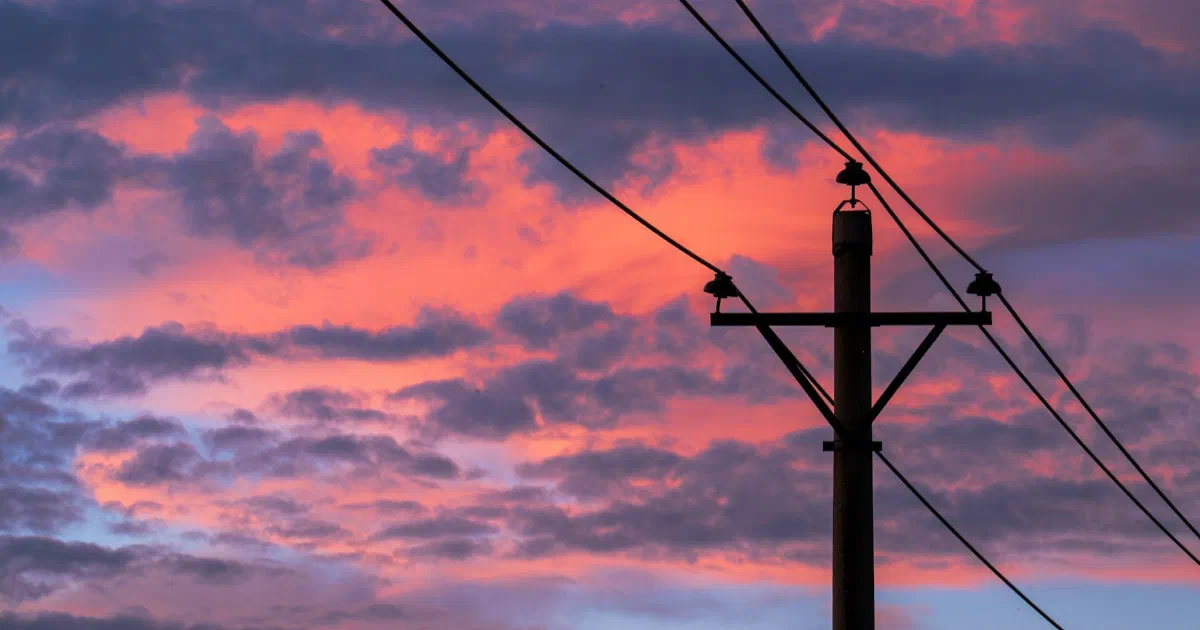 Wooden utility pole and power lines against pink and purple sunset clouds.