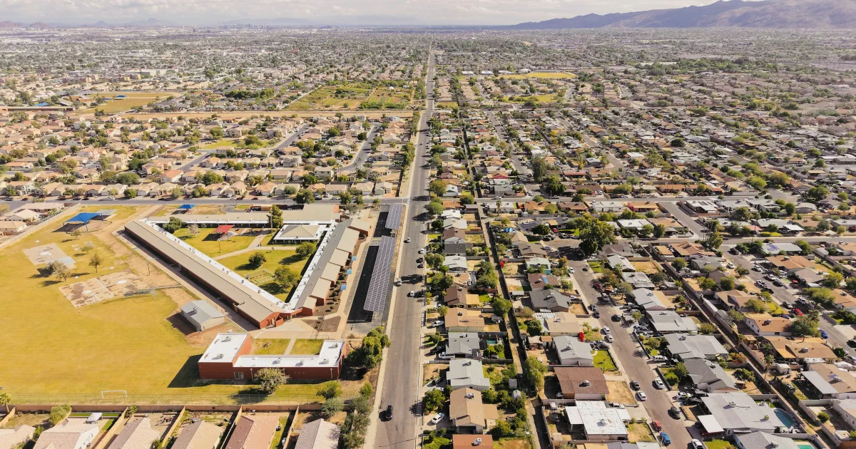 Aerial view of a dense suburban neighborhood with a long straight road and a school complex.