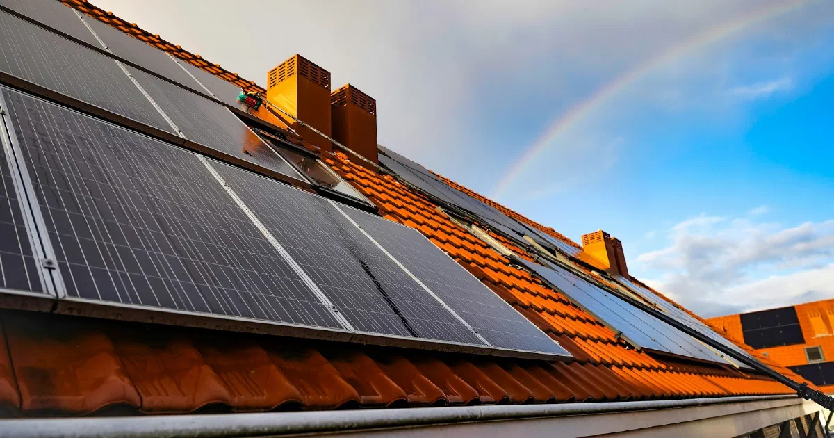 Solar panels on a clay tile roof with a faint rainbow in the sky behind.