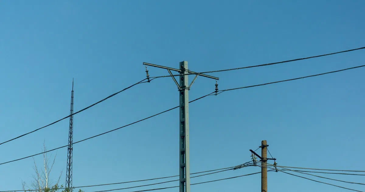 Wooden utility pole with power lines and a tall mast against a blue sky.