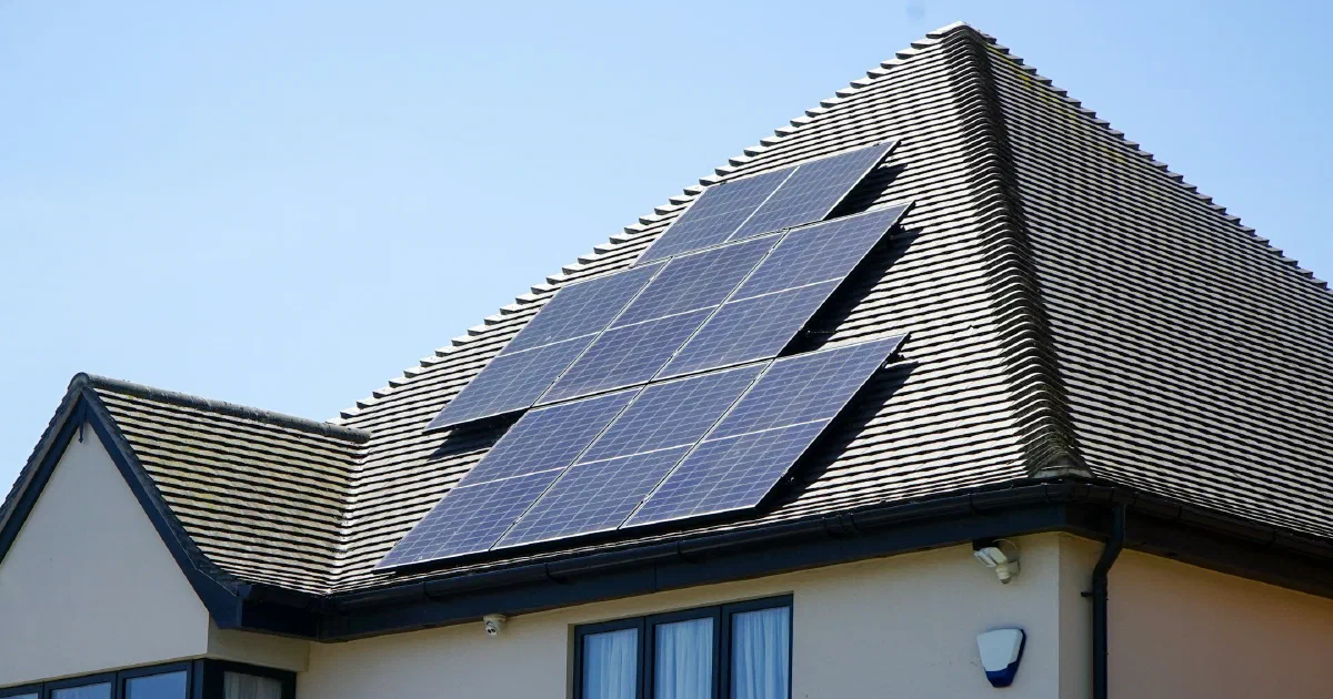 House with a group of solar panels on its tiled roof under a blue sky.