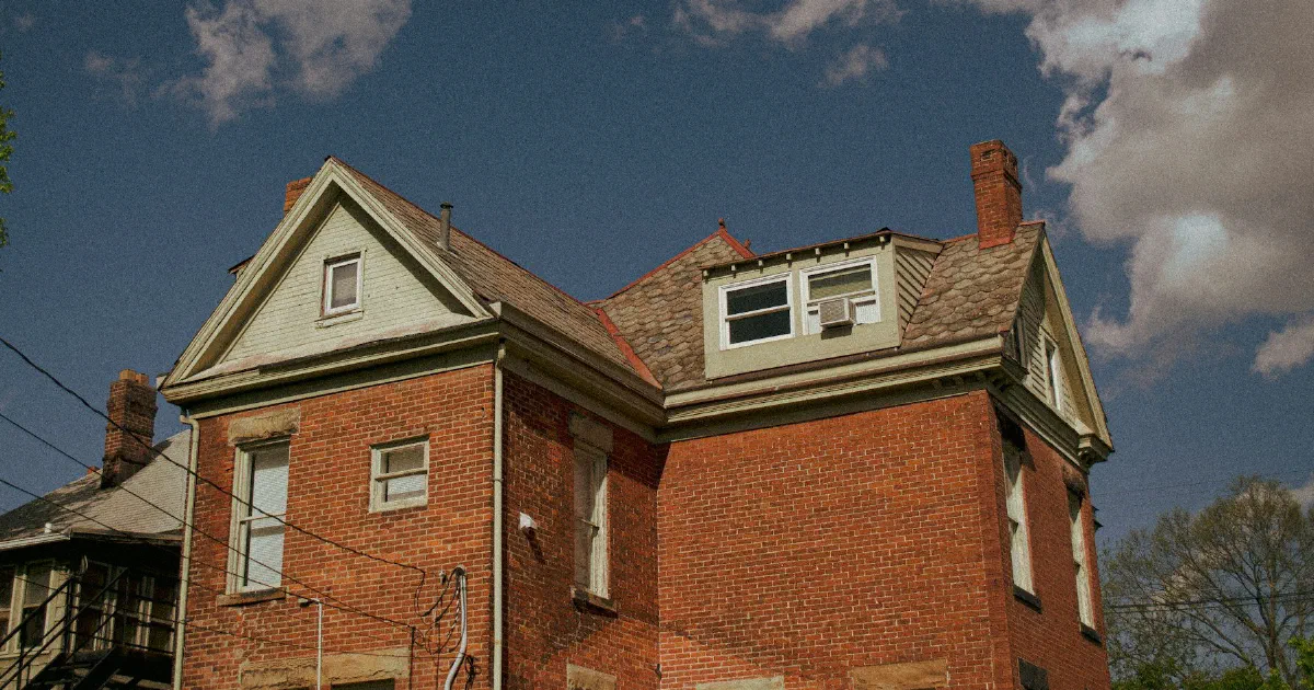 Red brick house with dormer windows under a deep blue sky with scattered clouds.