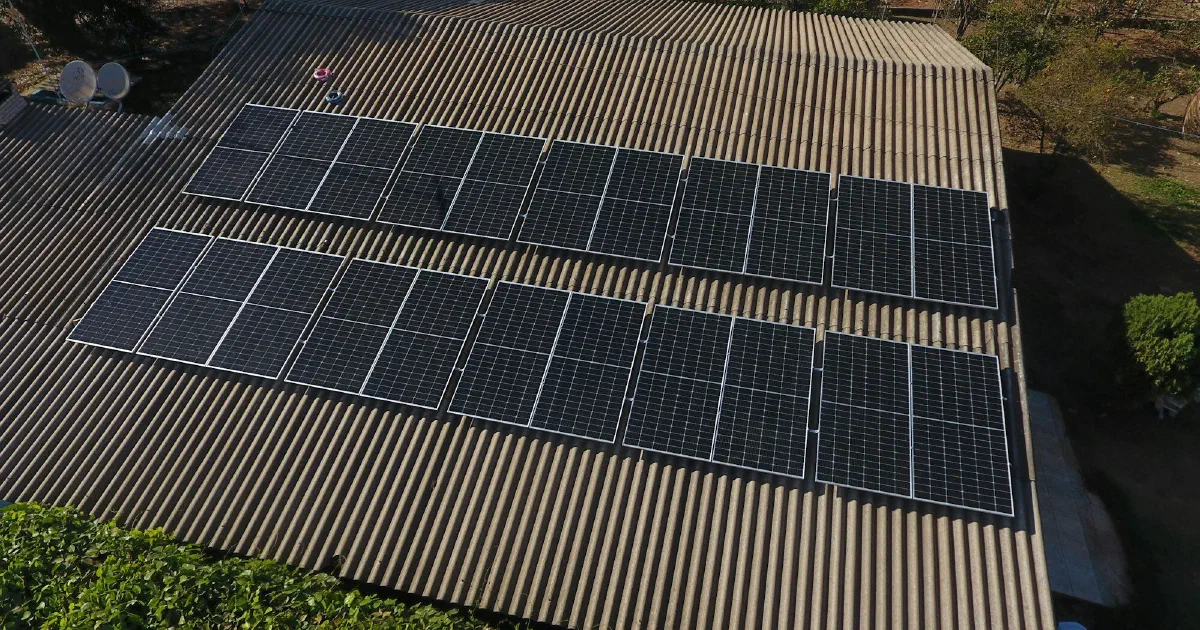 Rows of solar panels installed on a large corrugated metal roof, seen from above.
