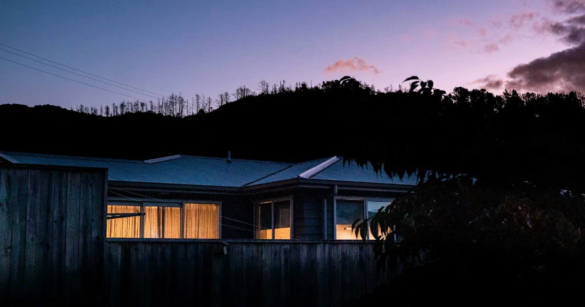 Single-story house with lit windows under a purple dusk sky.