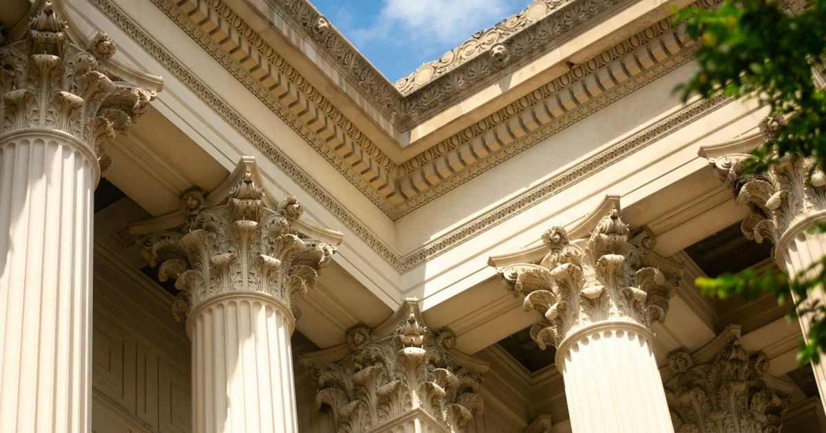 Corinthian columns and carved cornice of a neoclassical building against a blue sky.