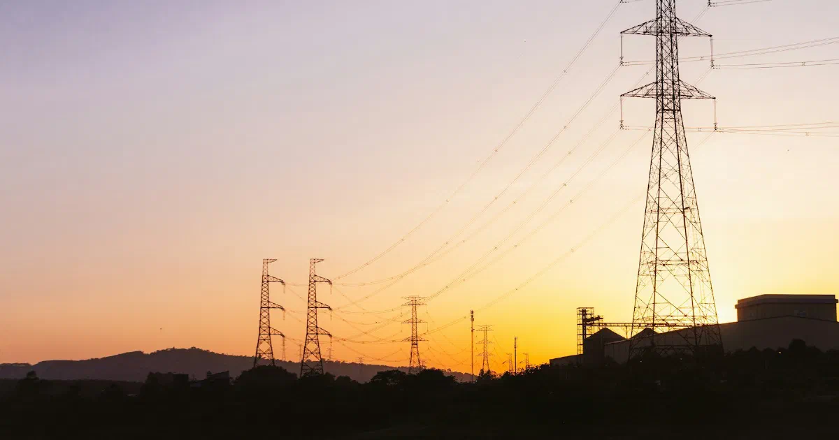 Transmission towers silhouetted at sunset with hills on the horizon.