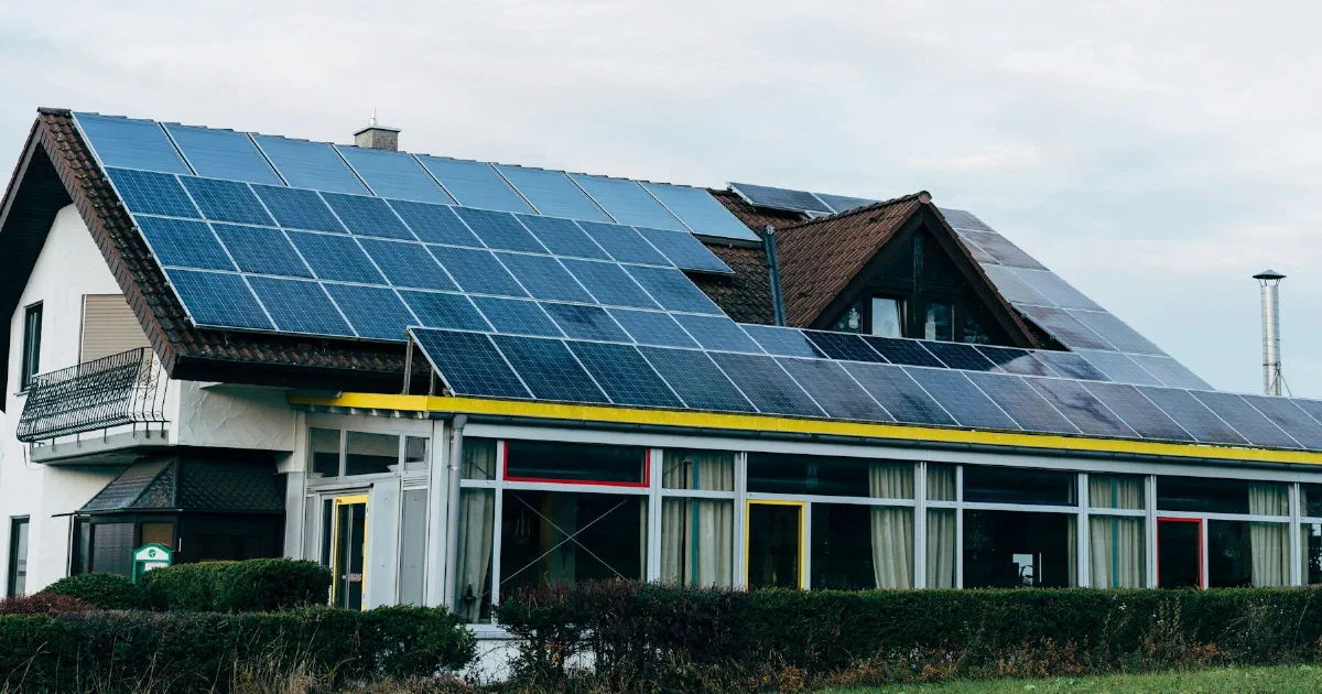 Large building with a steep roof covered in solar panels under an overcast sky.