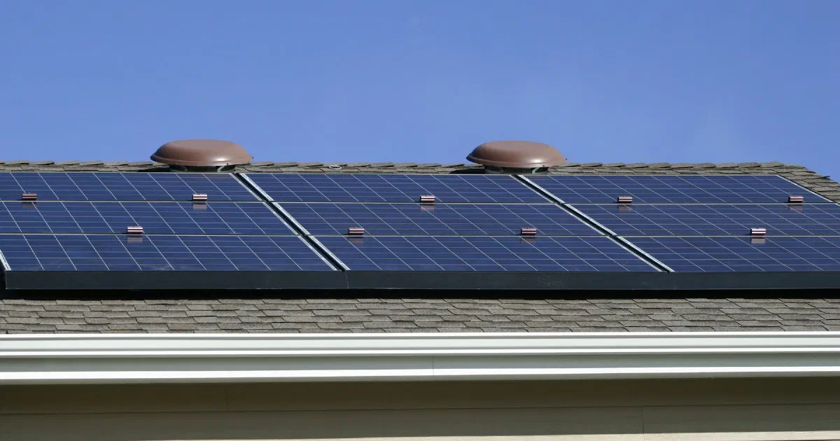 Solar panels mounted on the shingle roof of a house under a clear blue sky.