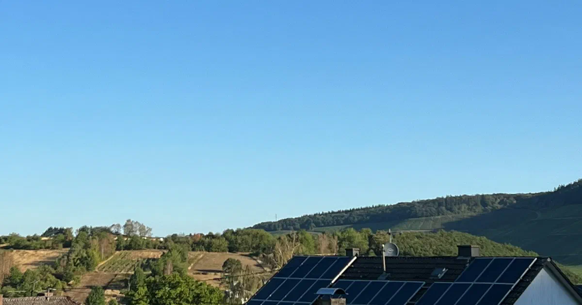 Rooftop solar panels in the foreground with wooded hills and blue sky behind.
