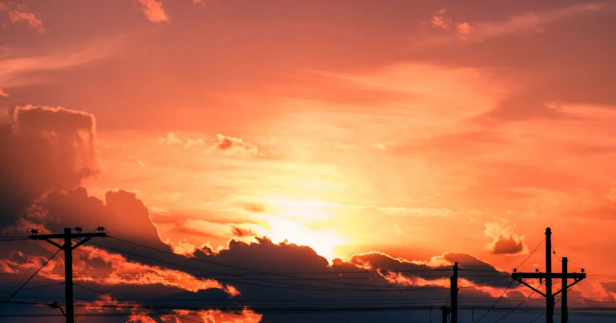 Utility poles silhouetted against a bright orange sunset with dark clouds.