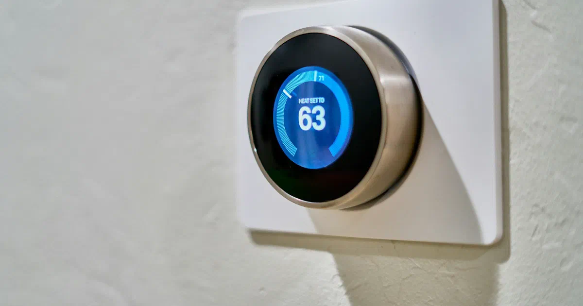 Round smart thermostat on a white wall showing a heat setting of 63 degrees.